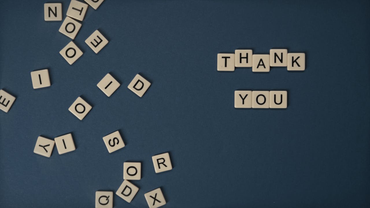 services-03 Top view of scattered Scrabble tiles with Thank You spelled out on blue surface.