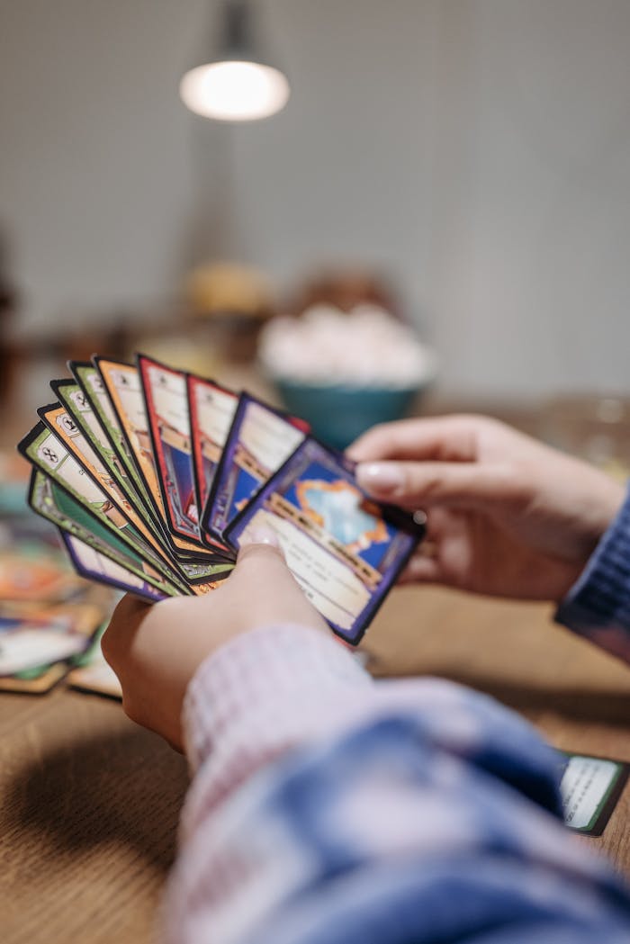 about-us-02 Close-up of hands holding a fan of playing cards indoors with warm lighting.