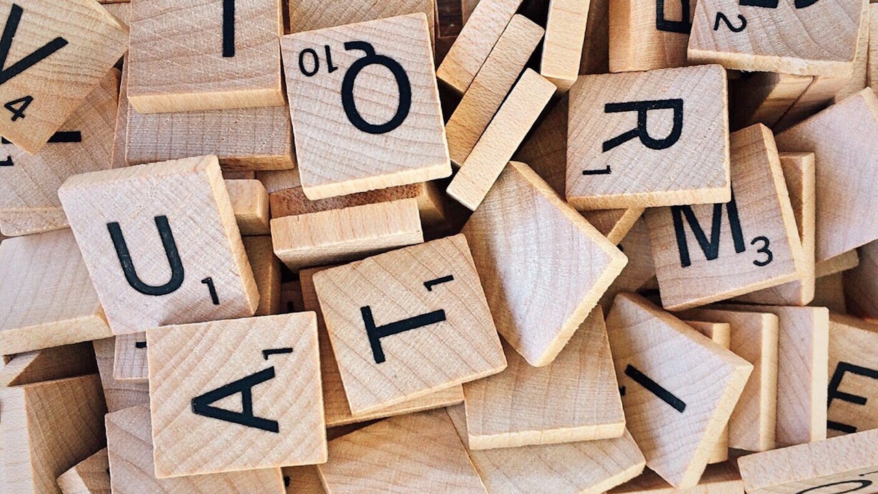 services-02 Close-up of wooden Scrabble tiles showcasing letters and numbers for word games.